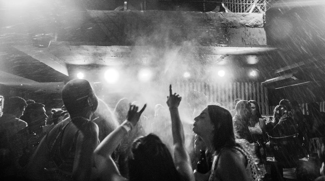 A dynamic black and white image captures a vibrant nightclub crowd dancing amidst smoke and lights.